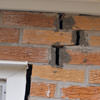 A brick wall displaying stair-step cracks and messy tuckpointing on a Trenton home
